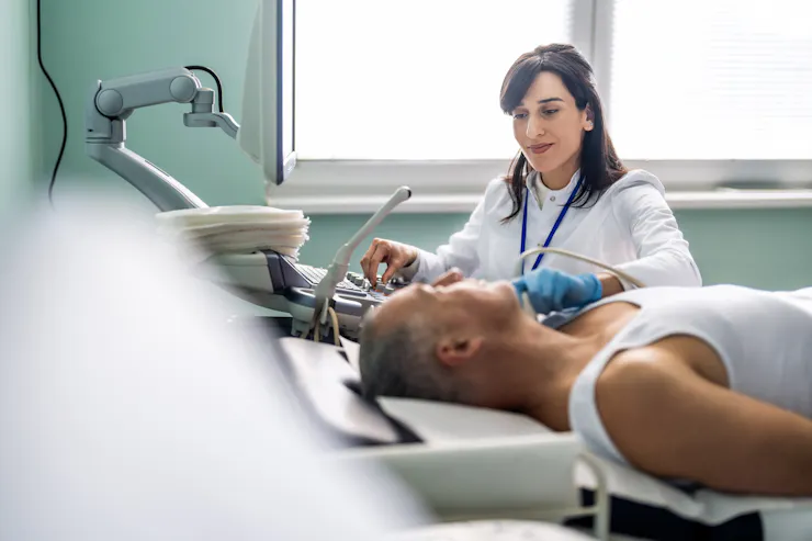 Patient lying on exam table as ultrasound technician places instrument on their neck