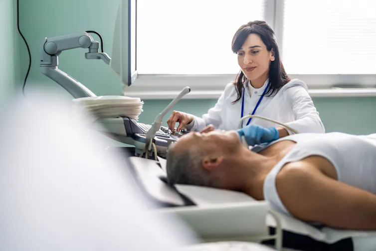 Patient lying on exam table as ultrasound technician places instrument on their neck