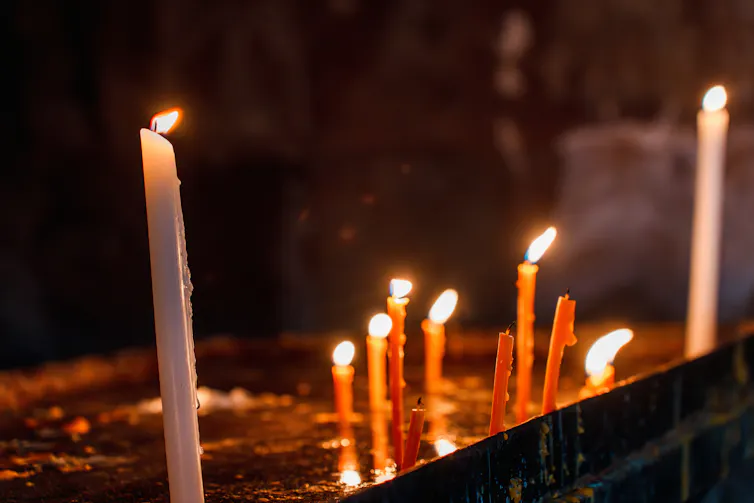Several candles flicker on a metal tray in a dark church.