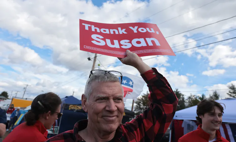 A man in a red and black checked shirt holds a sign aloft that says 'Thank You Susan.'