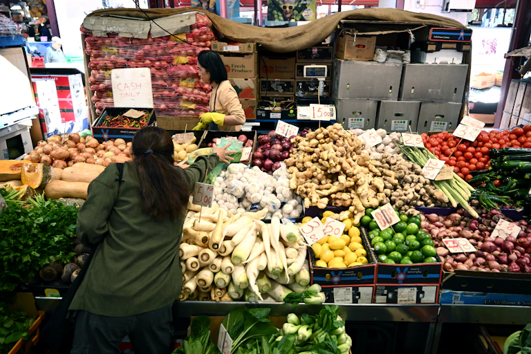A woman reaches for fruits and vegetables at a market.