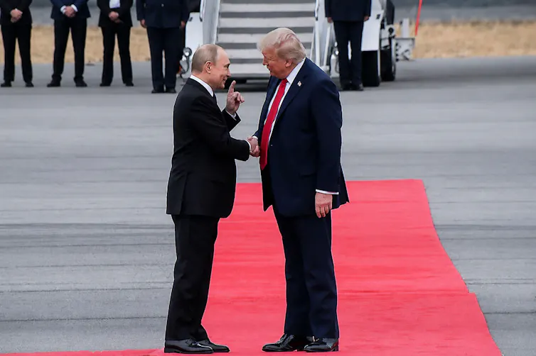 US president Donald Trump and Russian president Vladimir Putin stand togather on a red carpet in Alaska.