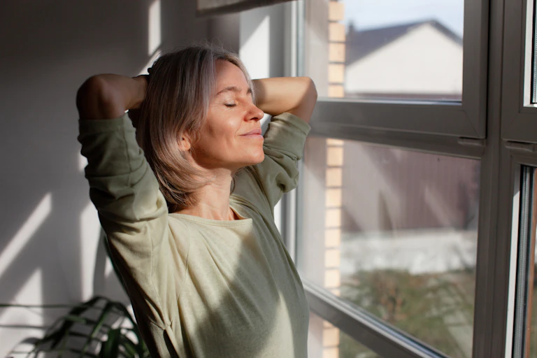 Belle femme d'âge moyen se relaxant avec les yeux fermés et le sourire dans le salon.