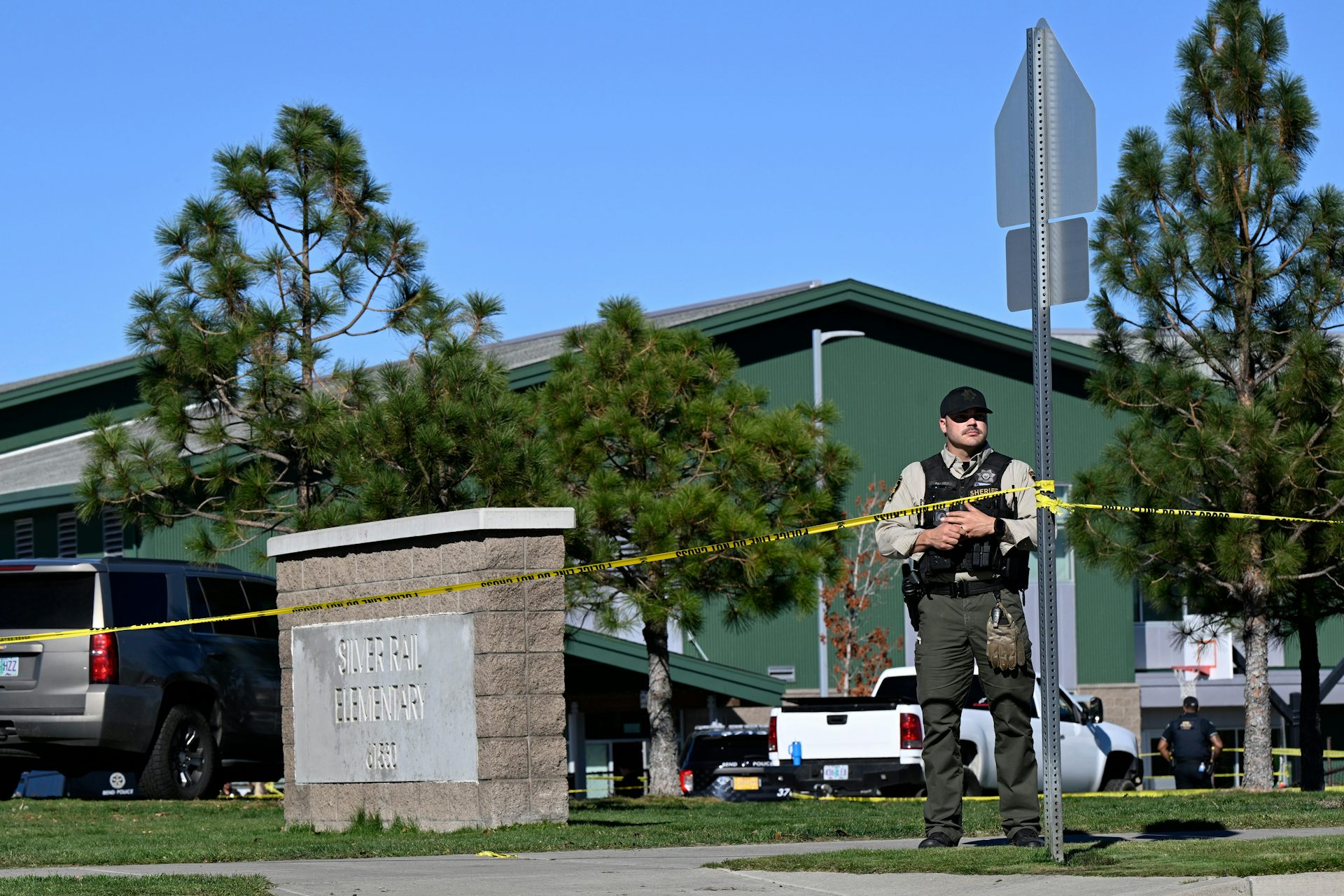 A uniformed law enforcement officer stands behind police tape outside a school building