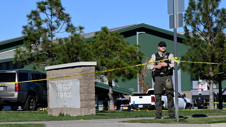 A uniformed law enforcement officer stands behind police tape outside a school building