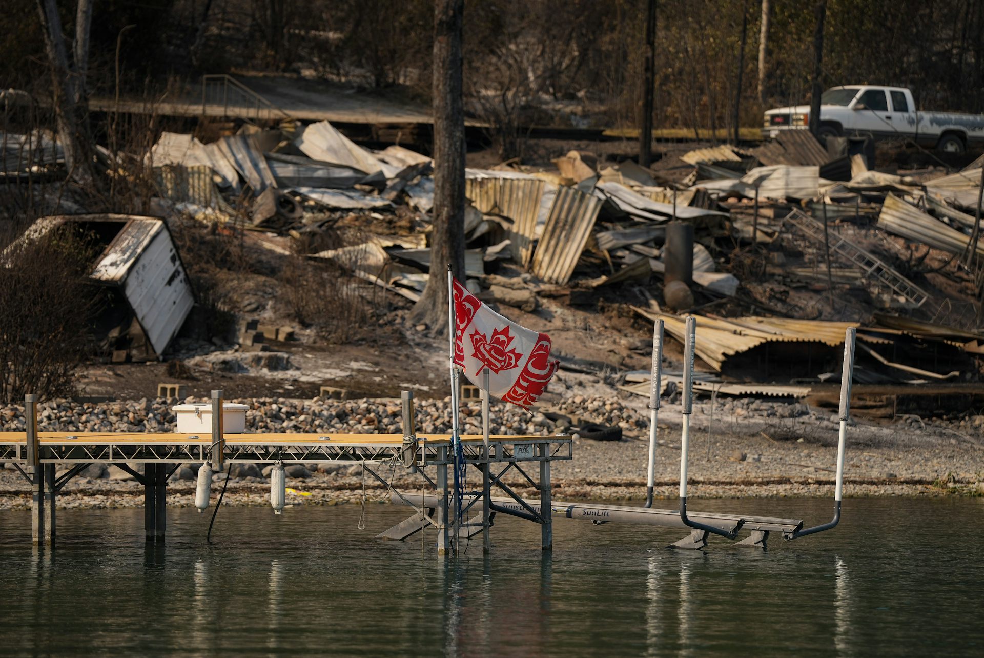 A Canadian flag with West Coast Indigenous design structuring the leaf and red sections flies on a burned out structure.