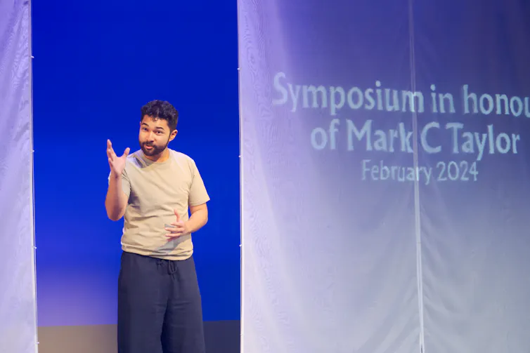 A man lectures, a projection says 'Symposium in honour of Mark C Taylor'