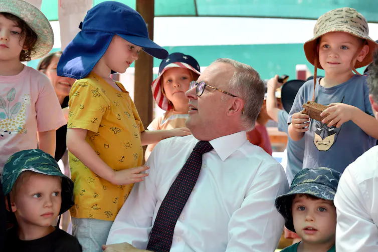 Anthony Albanese looks up at a child, surrounded by other children at a daycare centre