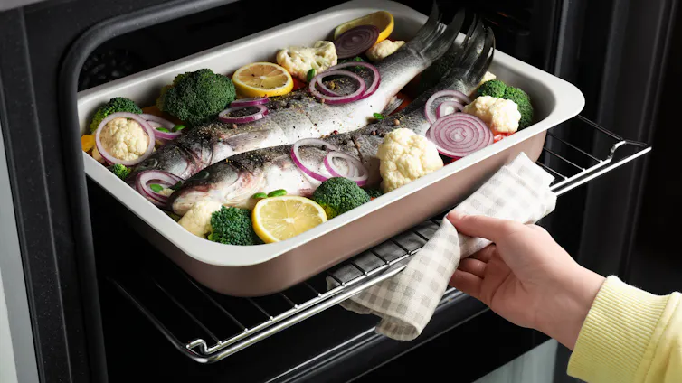 fish in baking tray with veg, oven gloved hand putting tray in black oven