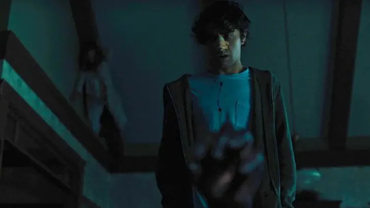 Dark movie still of man in foreground from a low angle and figure up at the ceiling