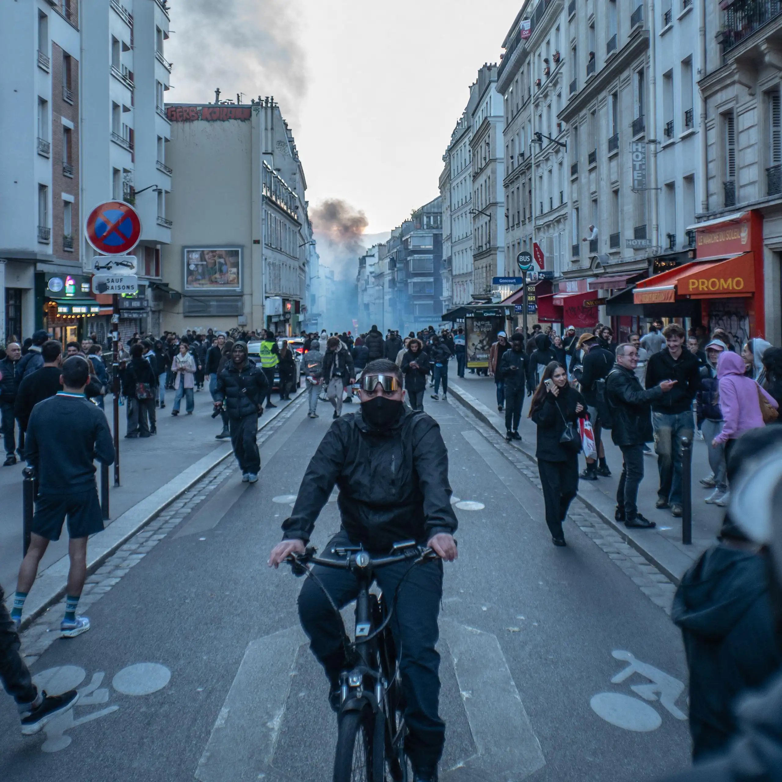 A man cycles along a Paris street in the aftemath of protests. Smoke can be seen rising in the distance.