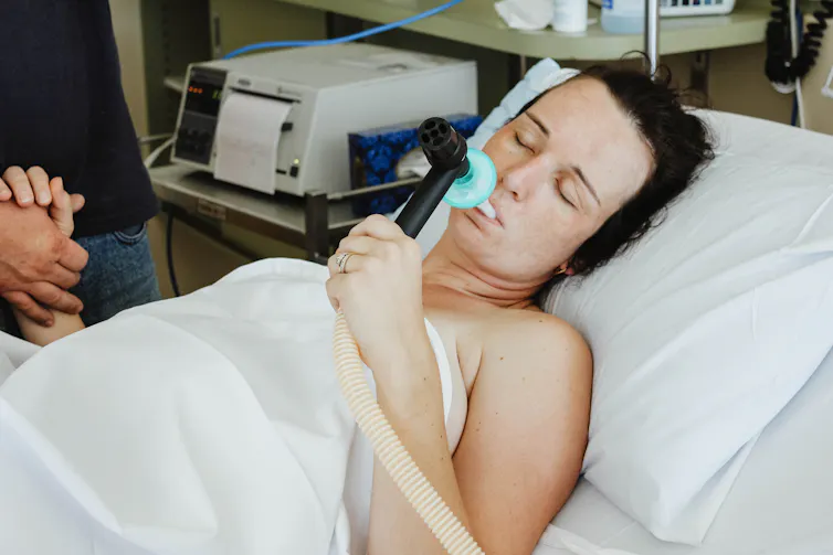 Woman using gas for pain relief during labor before giving birth with partner close by holding hand