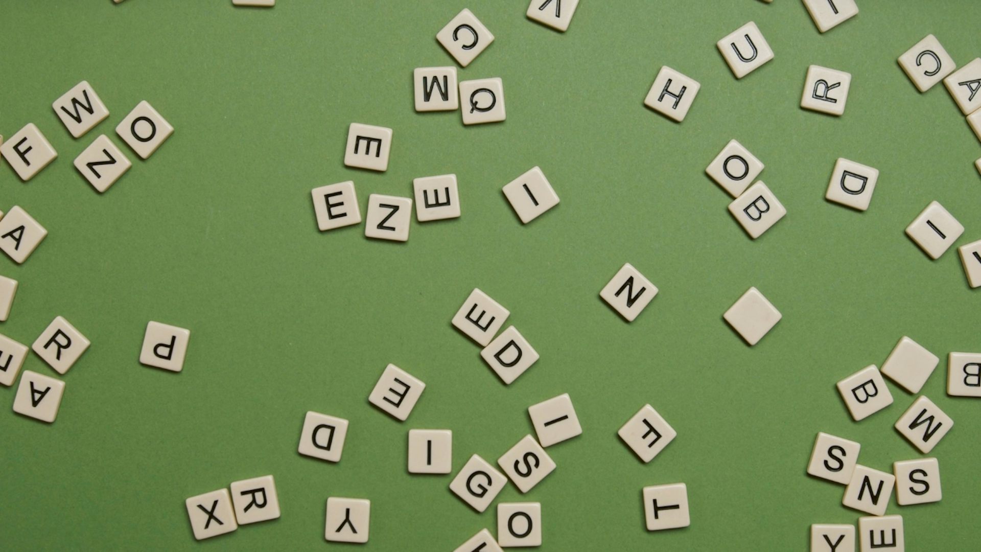 Scrabble pieces with letters scattered over a plain green background
