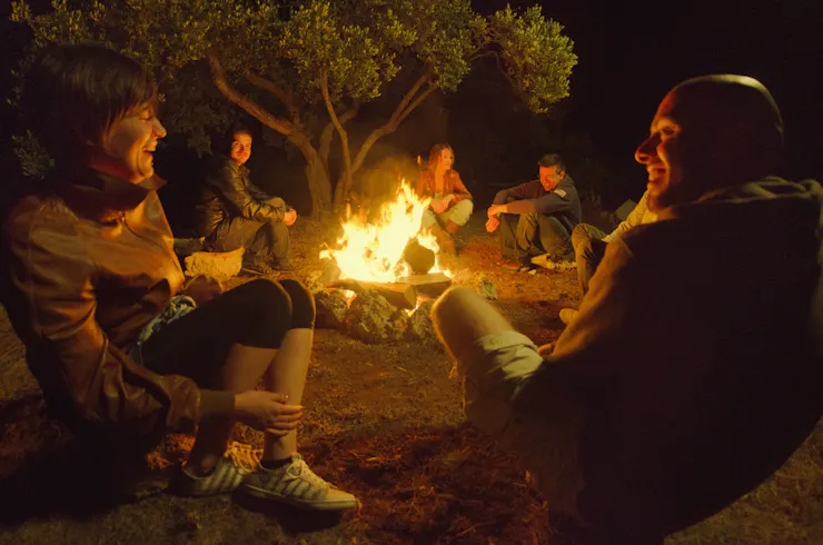 A group of people sitting around a campfire at night.