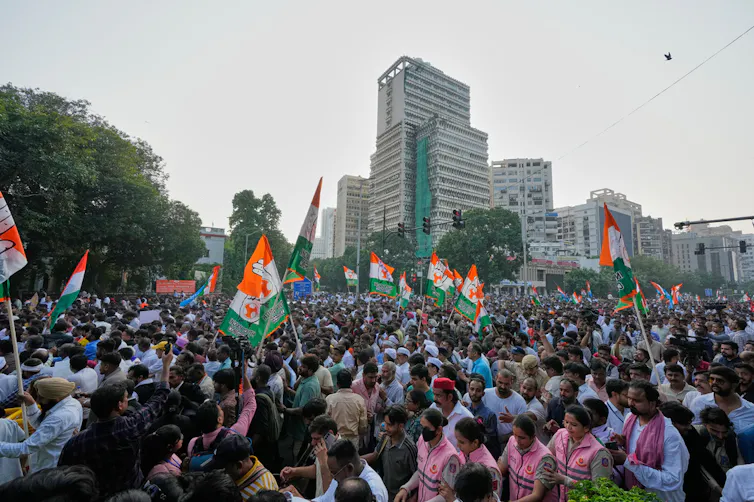 A crowd of protesters holding India's national flag walks in a procession on the streets.