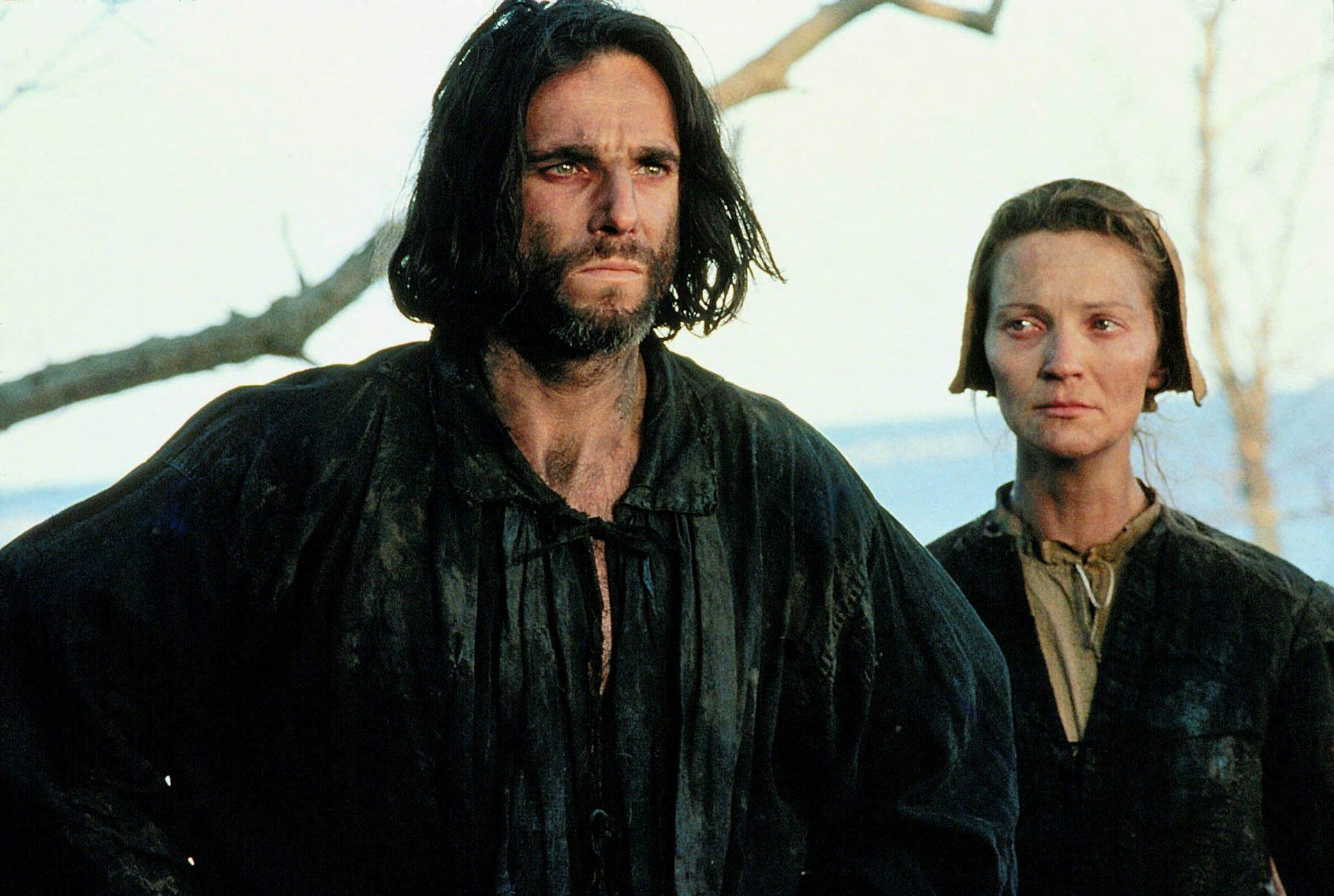 A man and a woman standing sombrely next to one another, the wife looking wretched.