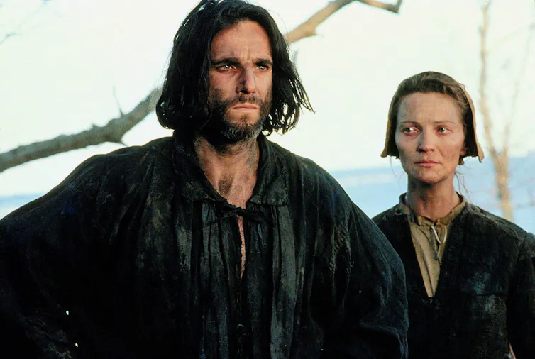 A man and a woman standing sombrely next to one another, the wife looking wretched.