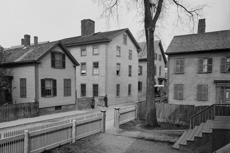 Black and white photo of old, clapboard colonial homes packed tightly together on a side street.