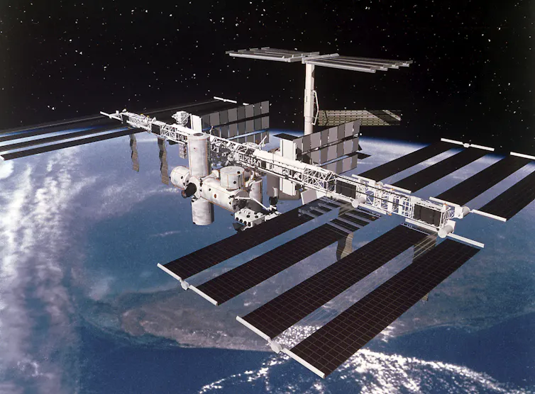 Black solar panels attached to while tubular structures hovering over Earth.