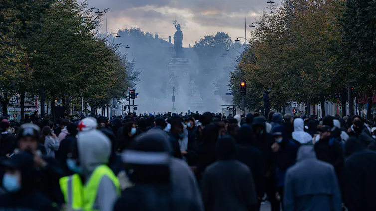 A large crowd fills the boulevard leading to Place de la République; the Monument to the Republic is shrouded in tear gas.