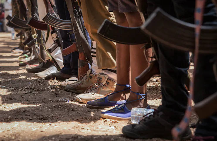 A line of young people, shown from the waist down, hold guns at their sides