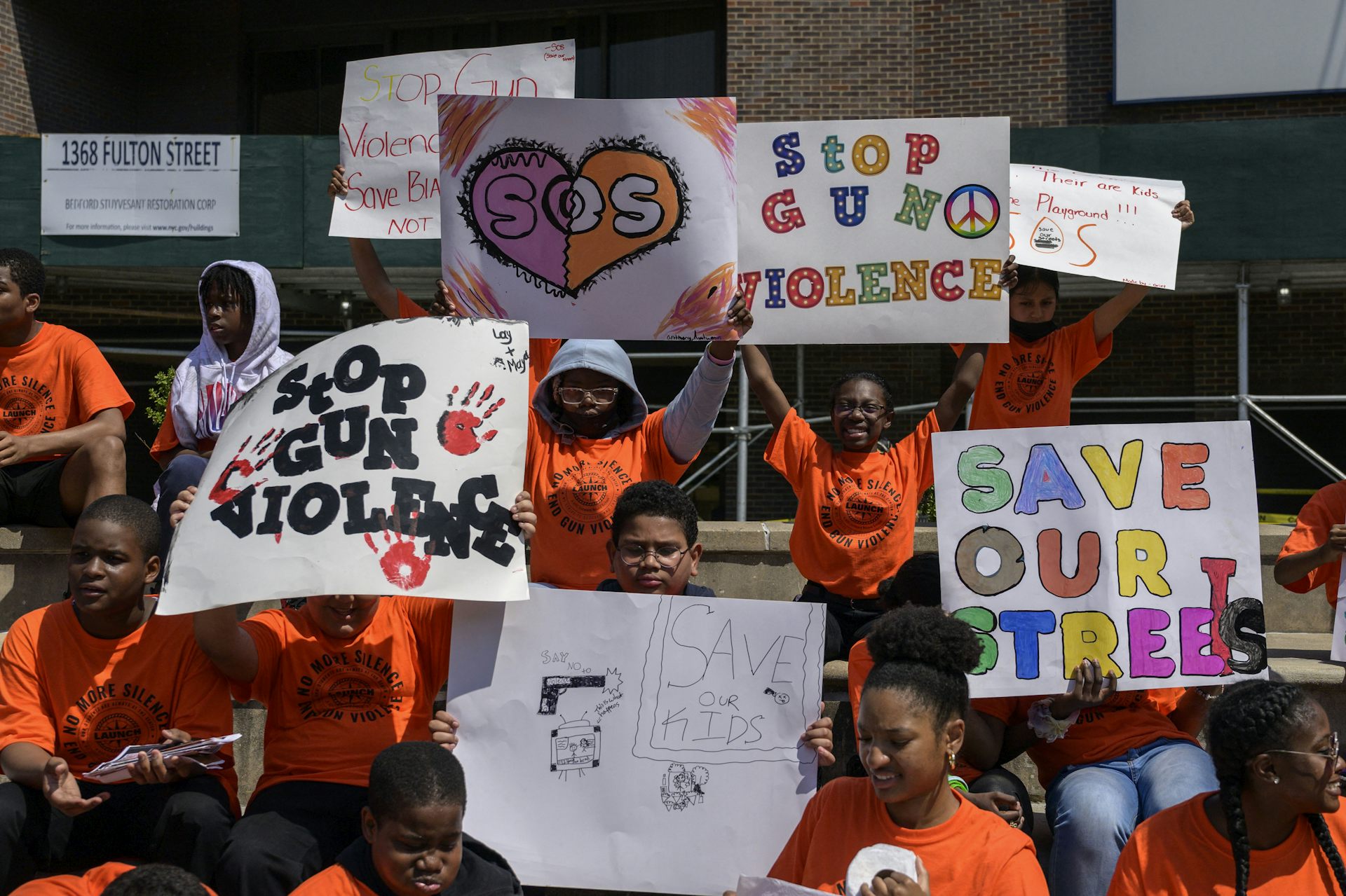 Students in orange T-shirts hold handmade signs reading 
