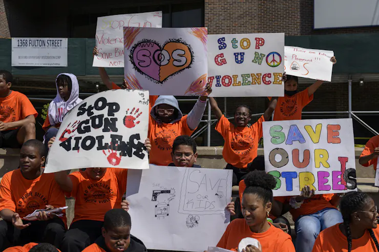 Students in orange T-shirts hold handmade signs reading