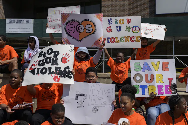 Students in orange T-shirts hold handmade signs reading