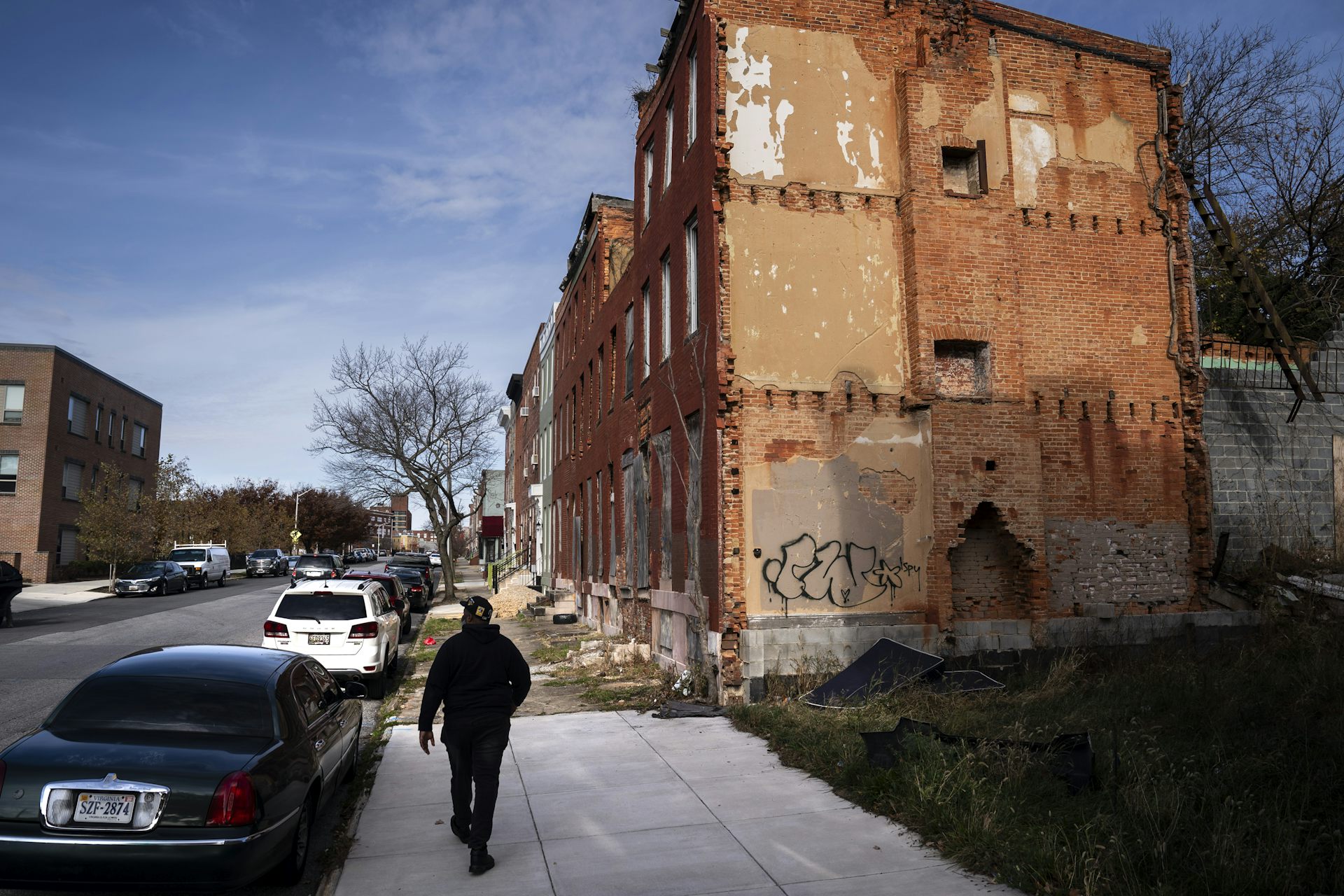 A man walks along a sidewalk past a row of vacant brick buildings.