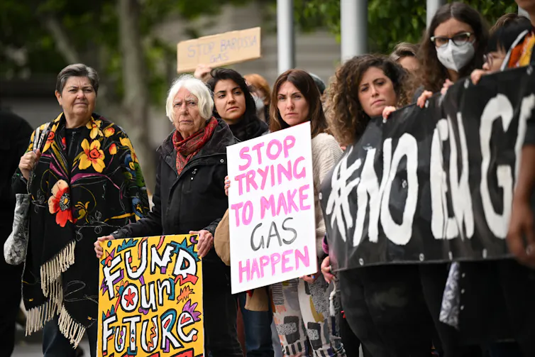 A crowd of people holding signs protesting again the development of new gas projects.