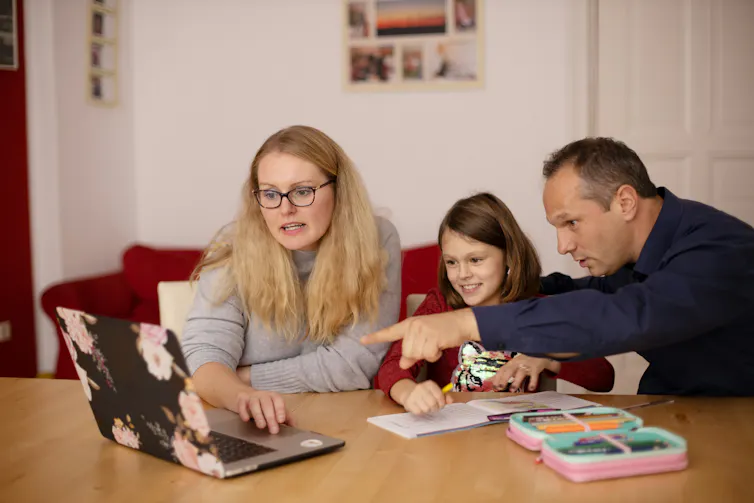 Parents sit at a table either side of their daughter to help her study