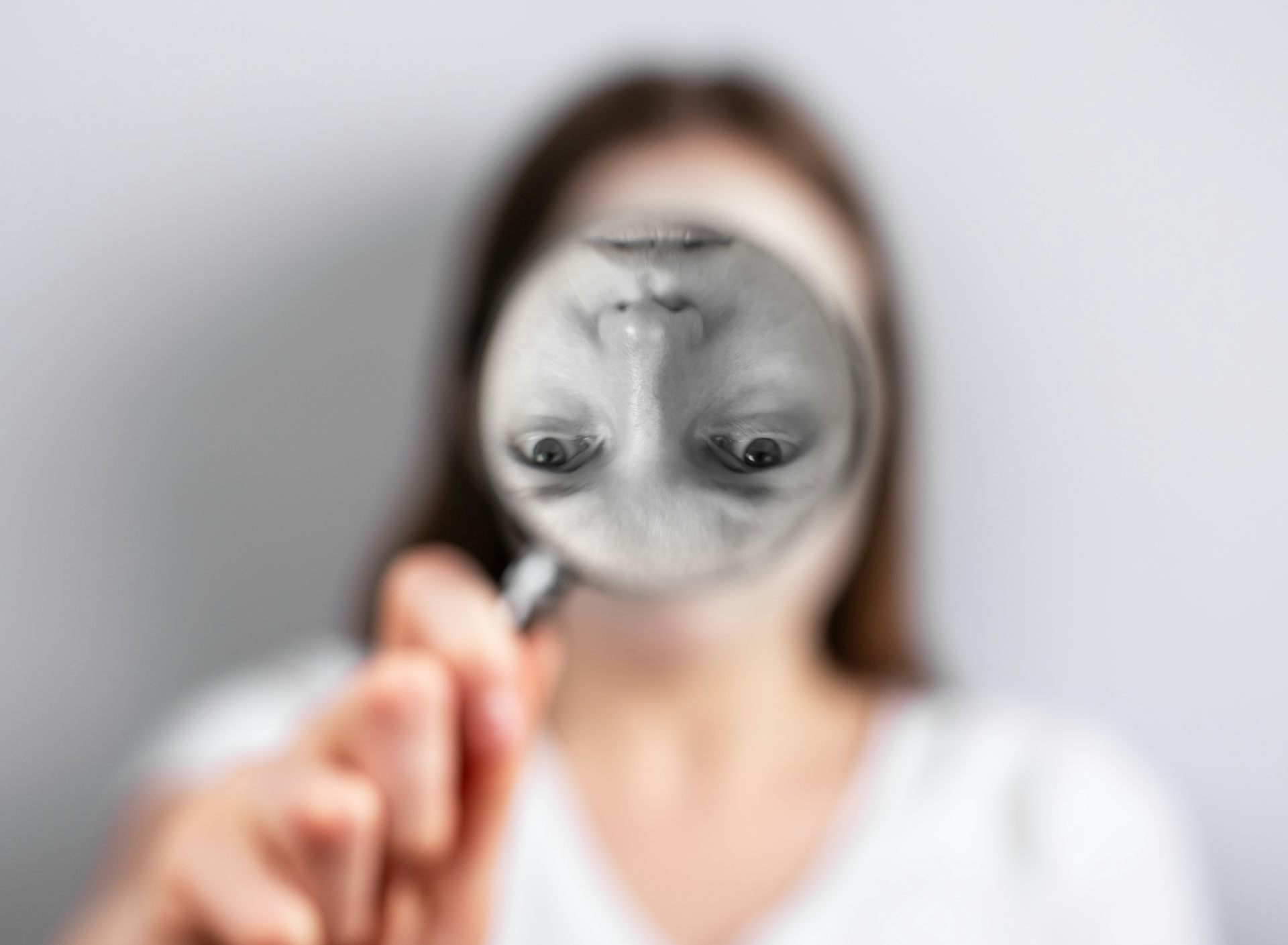 A woman peers through a magnifying glass. Her face is reflected in it, but it is upside down and in black and white.