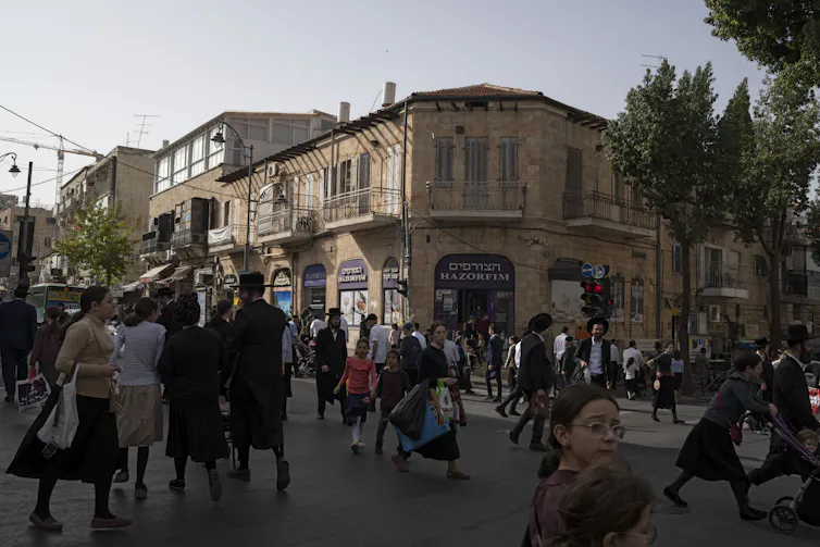 A busy shopping street with men and women in modest clothing.