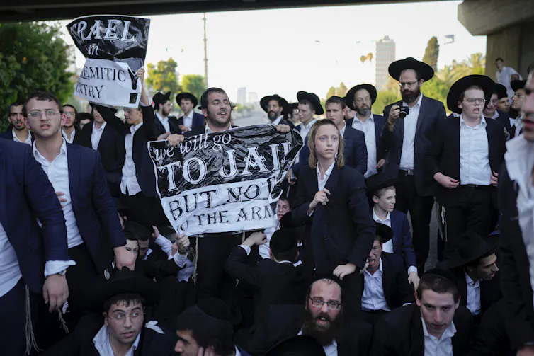Men in black suits and white shirts hold signs that say, 'We will go to jail, but not to the army.'