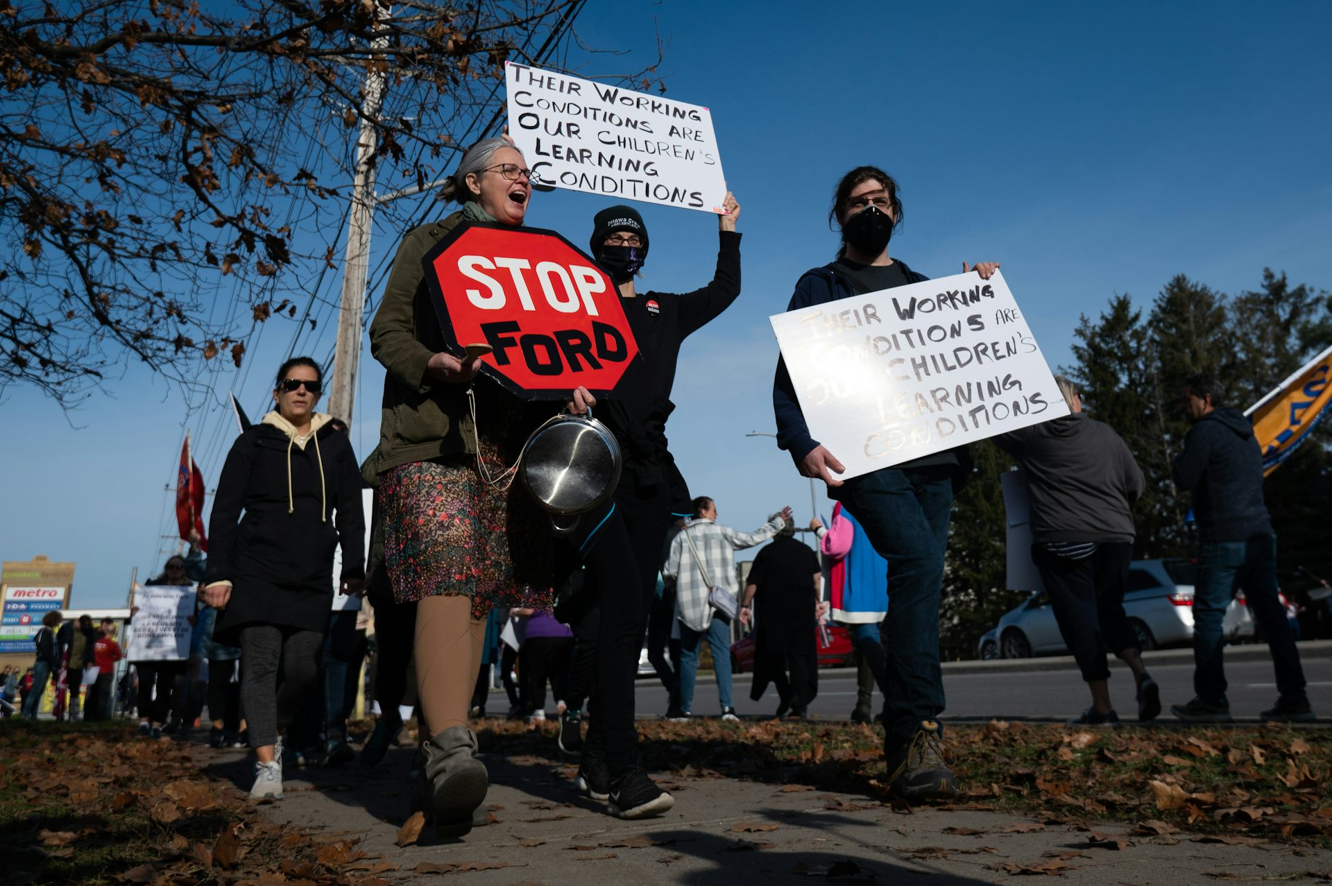 People march on a sidewalk, one with a stop sign that says stop Ford.