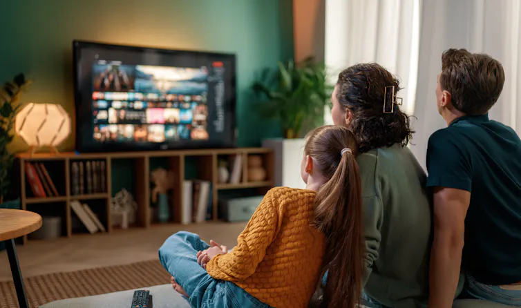 A mother and father watch a movie at home with their daughter.