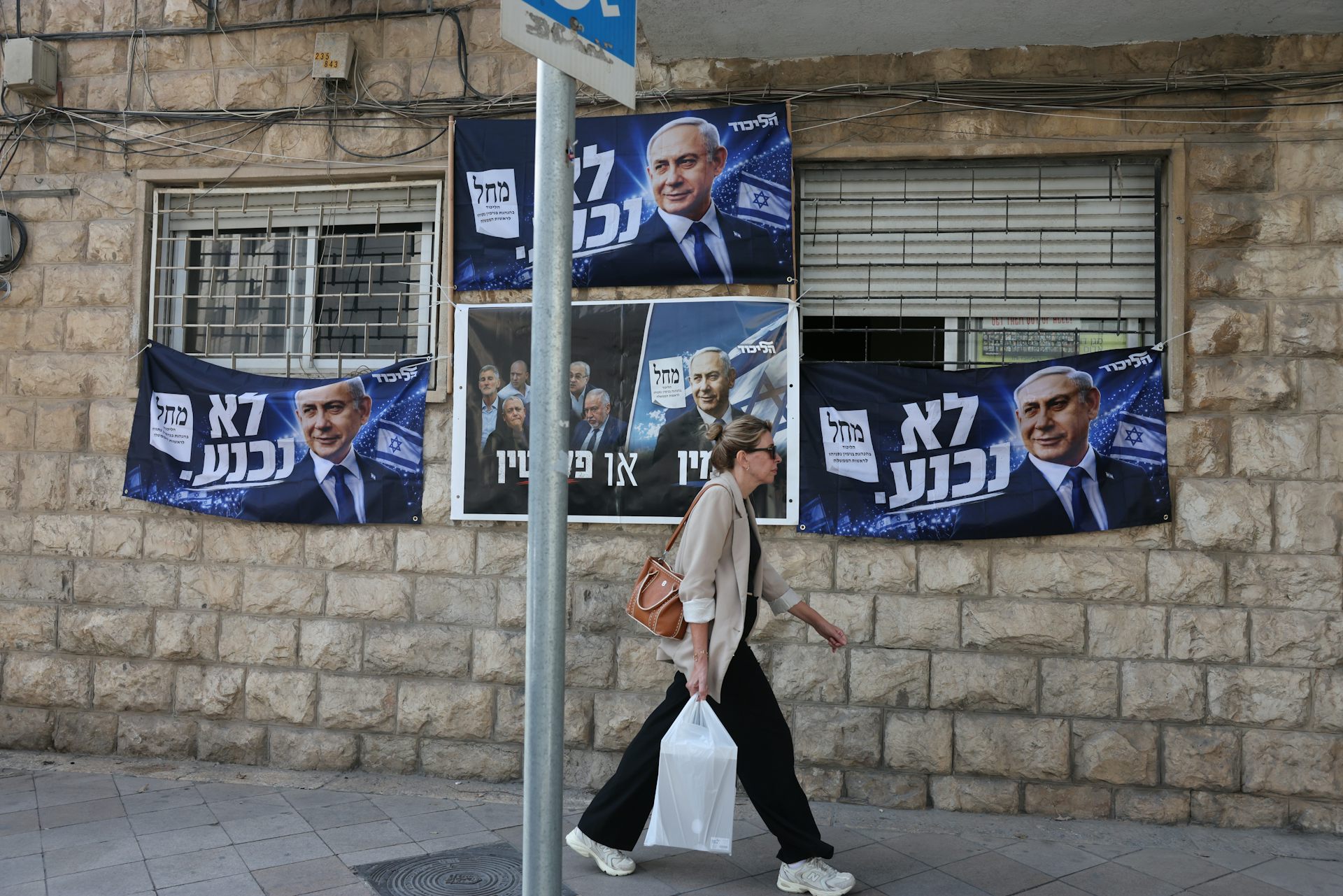 A woman passes an election billboard of Benjamin Netanyahu with a Hebrew slogan reading: 'will not surrender'.