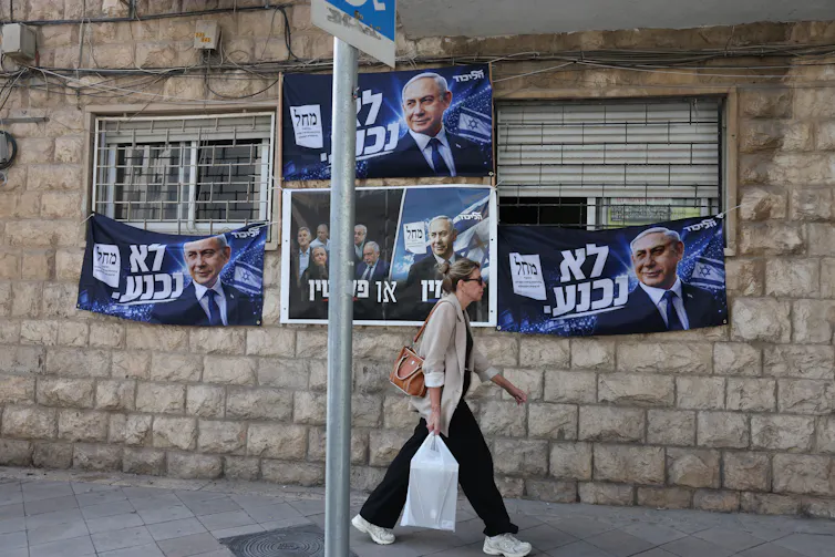A woman passes an election billboard of Benjamin Netanyahu with a Hebrew slogan reading: 'will not surrender'.
