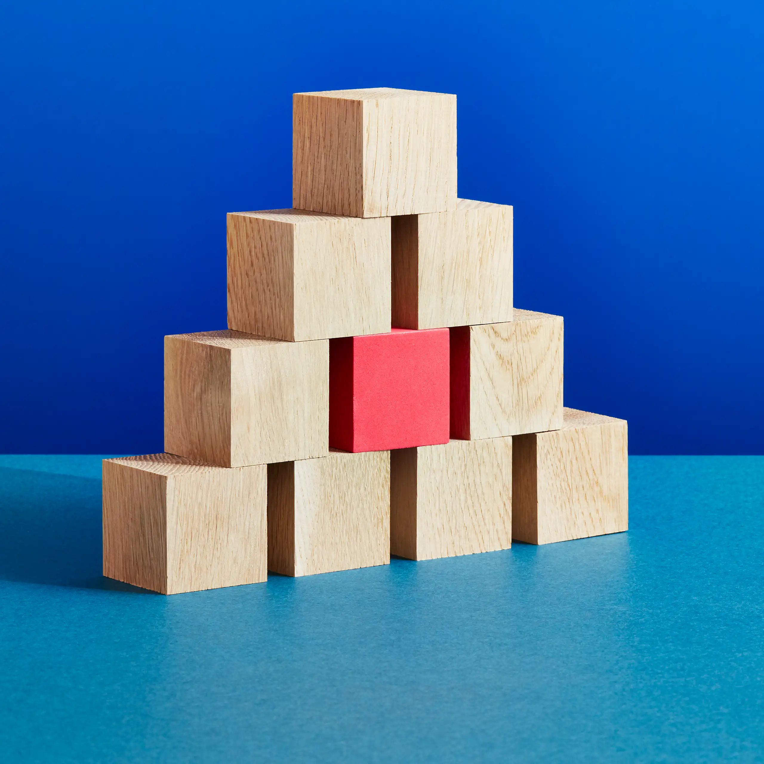 a pyramid of wooden building blocks, one on top of two on top of three on top of four, with the middle of the three colored red
