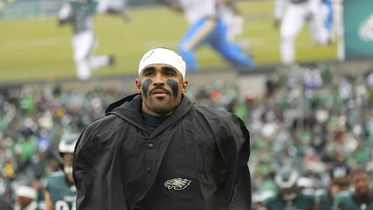 Football player wearing black jacket in stadium with fans wearing green