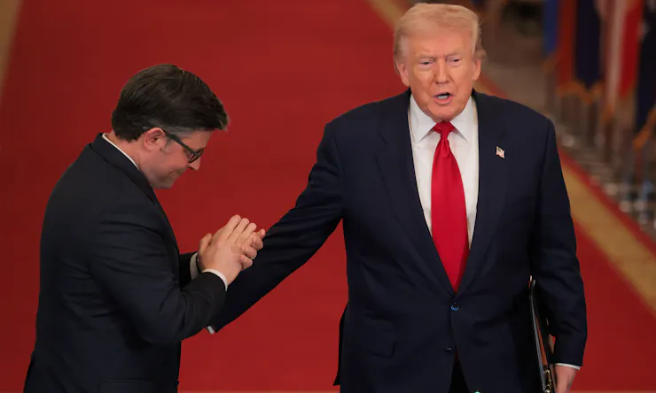 Two men in dark suits, with one appearing to honor the other with a bowed head and clasped hands.