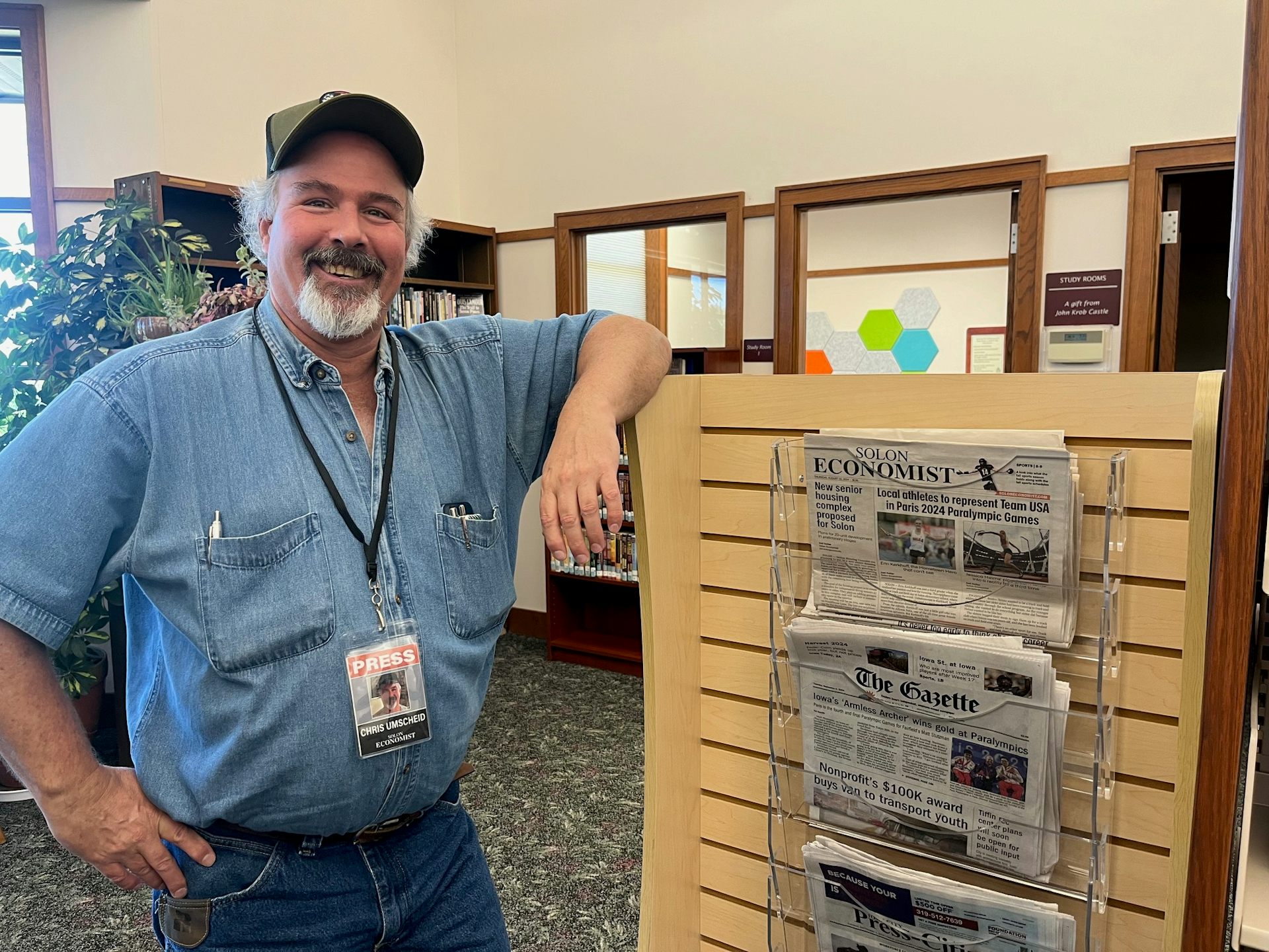 Chris Umscheid, editor of the Solon Economist in Iowa, stands next to a newspaper rack with print editions.
