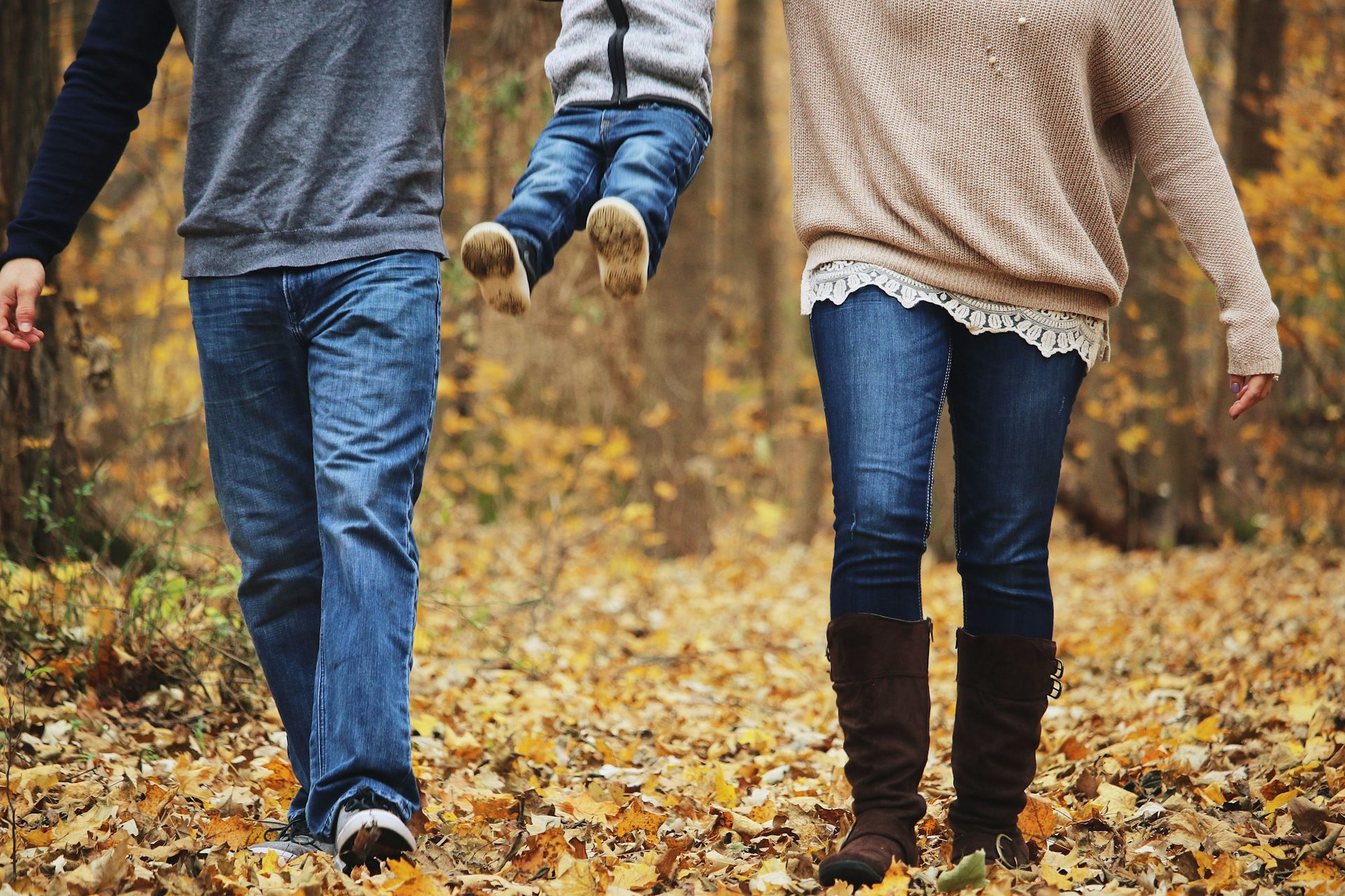 A child is swung into the air by their two parents while on a walk.