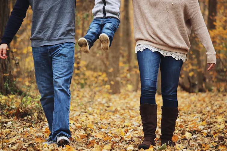 A child is swung into the air by their two parents while on a walk.