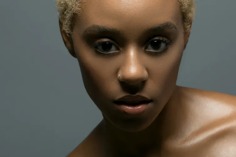 A young woman with dark eyebrows and bleached hair.