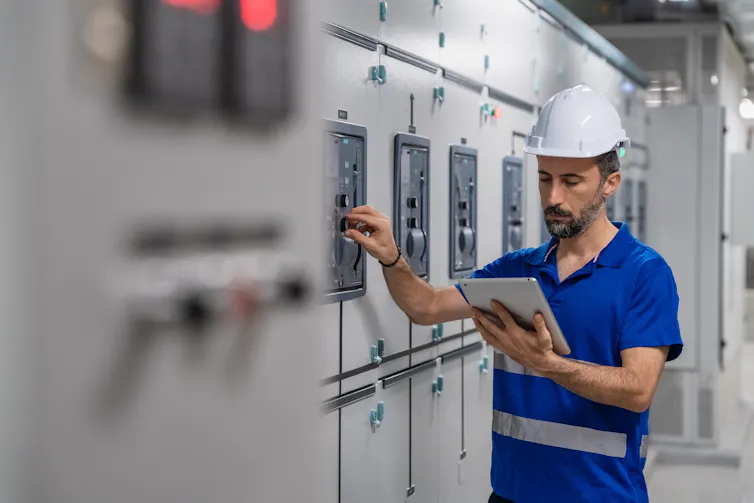 Electrical engineer adjusting power panel in control room for smart grid maintenance.