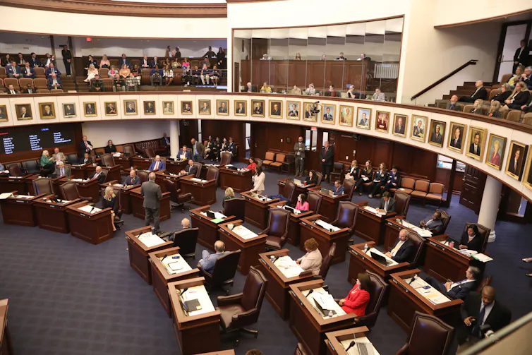 people at desks arranged in a semicircle with a balcony above them