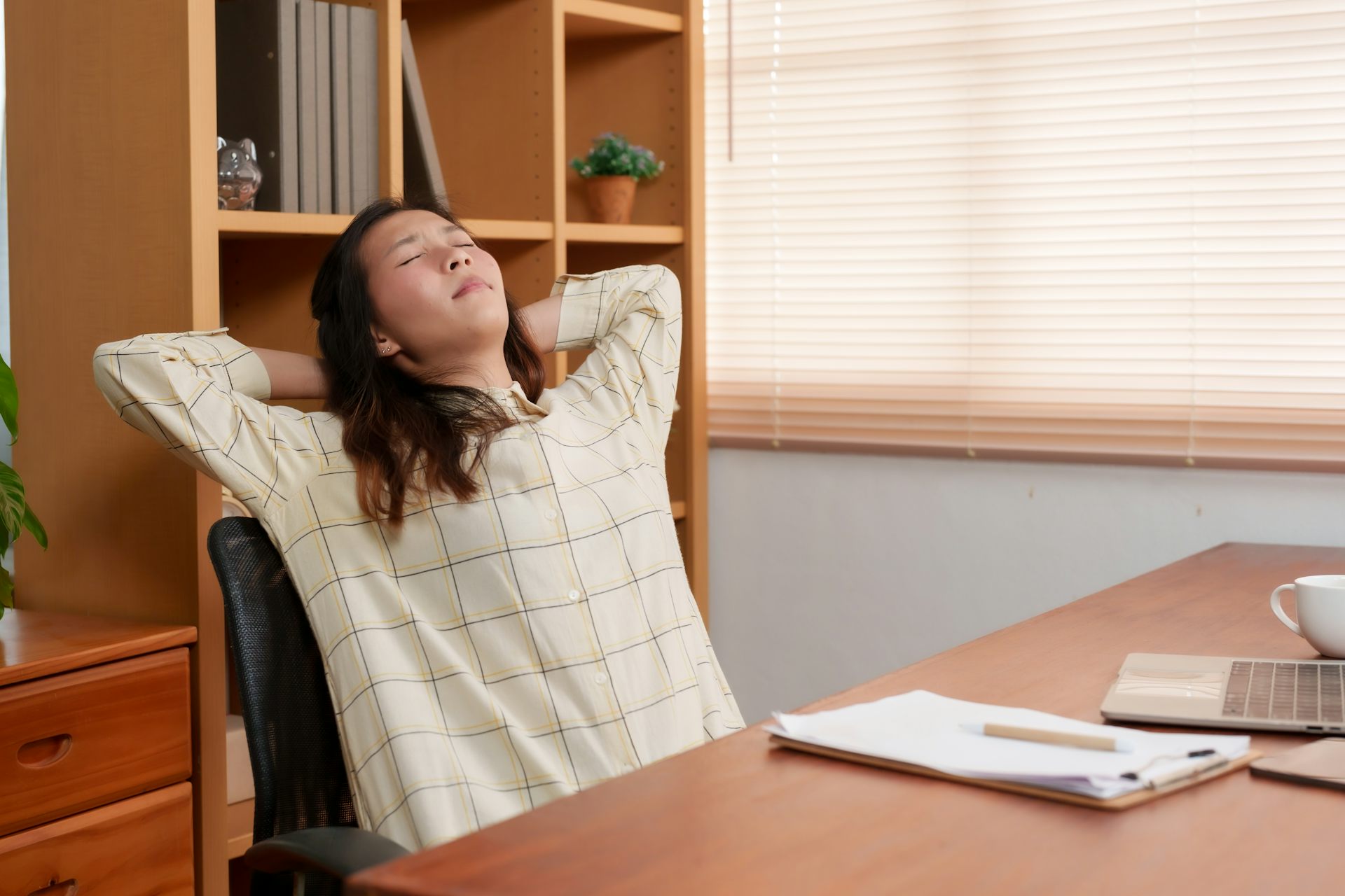 A woman sitting in an office chair stretches her upper back over the back of the chair.