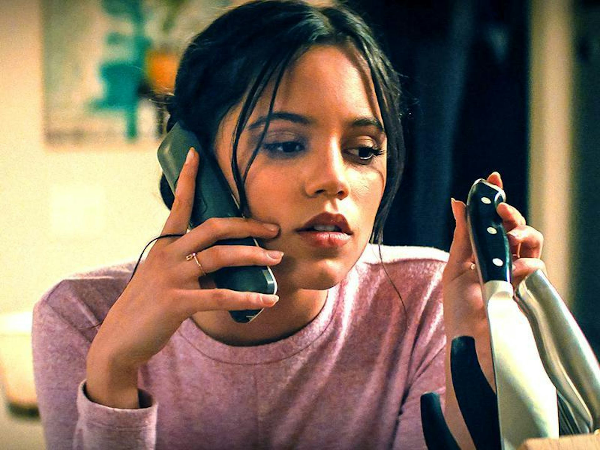 A woman holds a phone to her hear and in her other hand pulls a knife out of its holder.