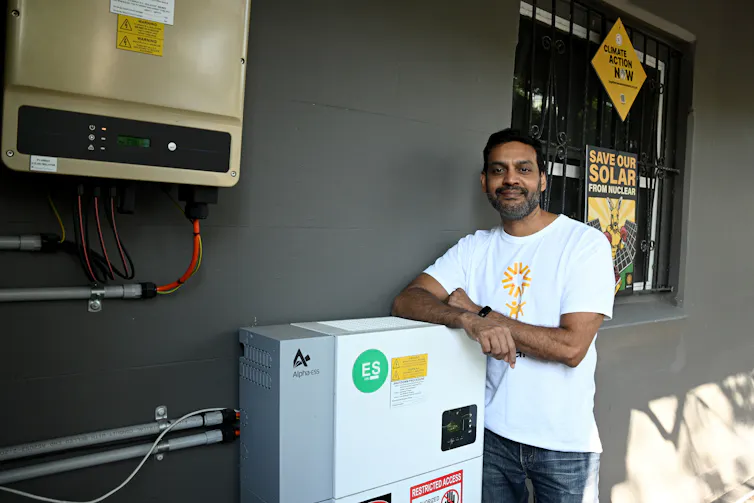 A smiling man with his solar battery system at his home.